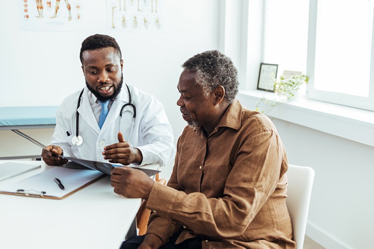 Black doctor in white coat speaking with a Black senior patient in an office