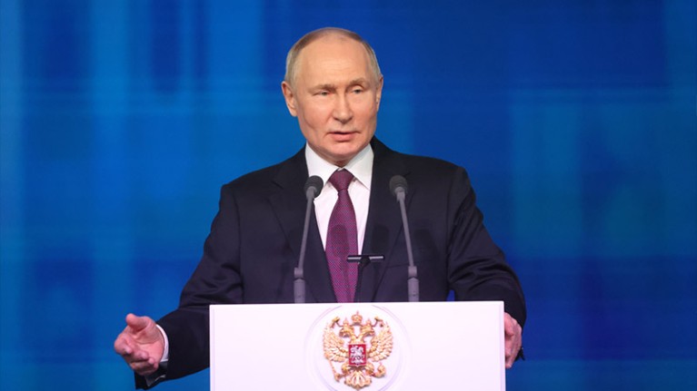 Vladimir Putin behind a lectern marked with a golden eagle crest.