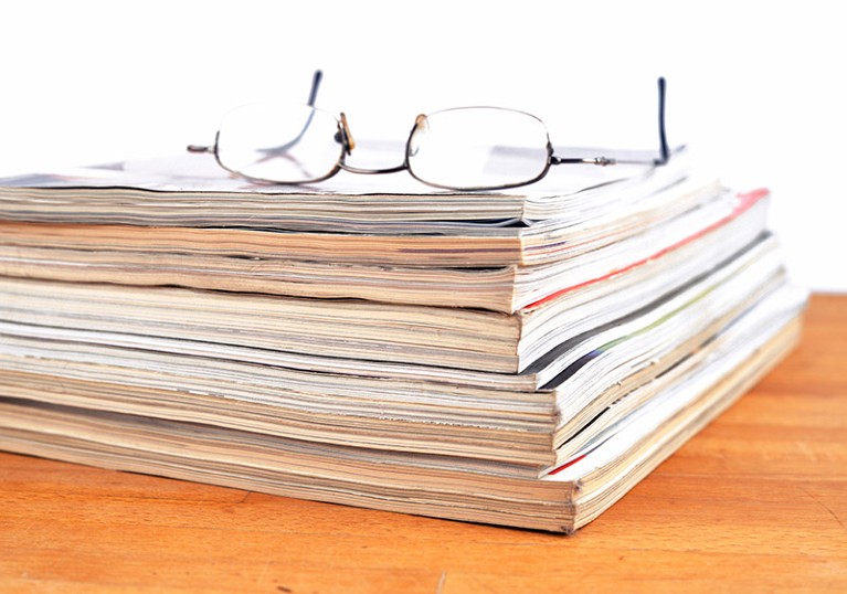 A pair of glasses rest on top of a stacked pile of journal magazines.