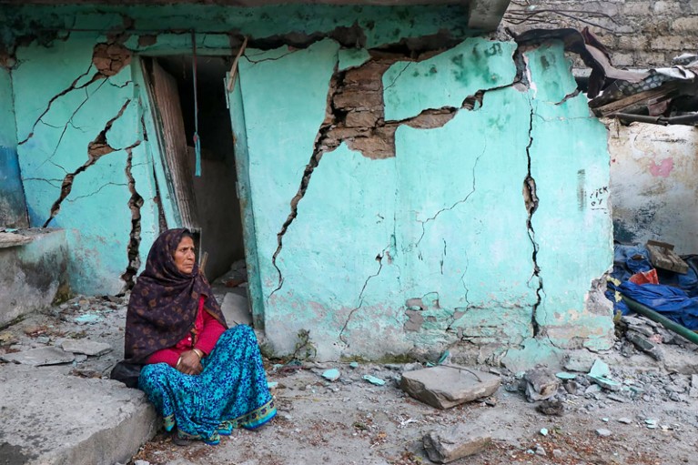 A woman sits beside a cracked wall of her house in India