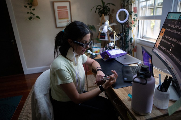 Lauren Nichols reads her blood oxygen levels and heart rate from a machine on her finger at her desk in her home
