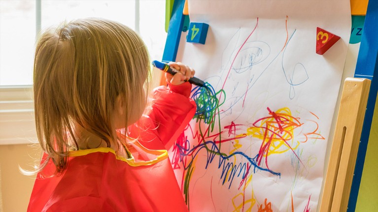 A young left handed child draws with a crayon on an easel.