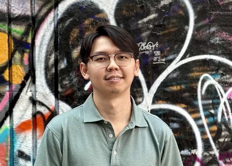 Portrait of Qimin Liu in front of a graffitied wall.
