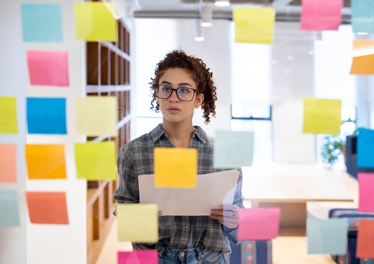 A person organizing ideas and thoughts with sticky notes on a glass wall.