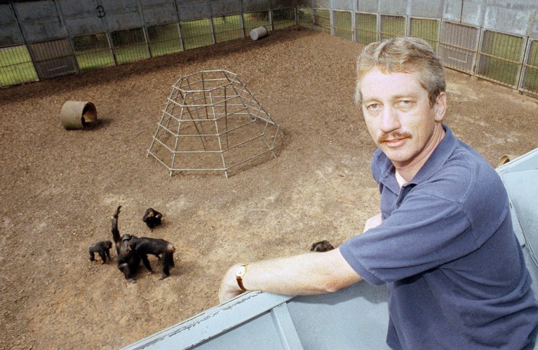 Frans de Waal poses for a portrait next to some primates in an enclosure