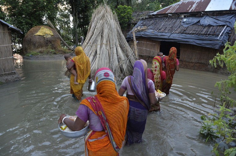Indian villagers carrying babies wade through flood waters after collecting relief food