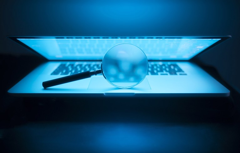 Uma lupa iluminada pela tela de um laptop parcialmente aberto no escuro.