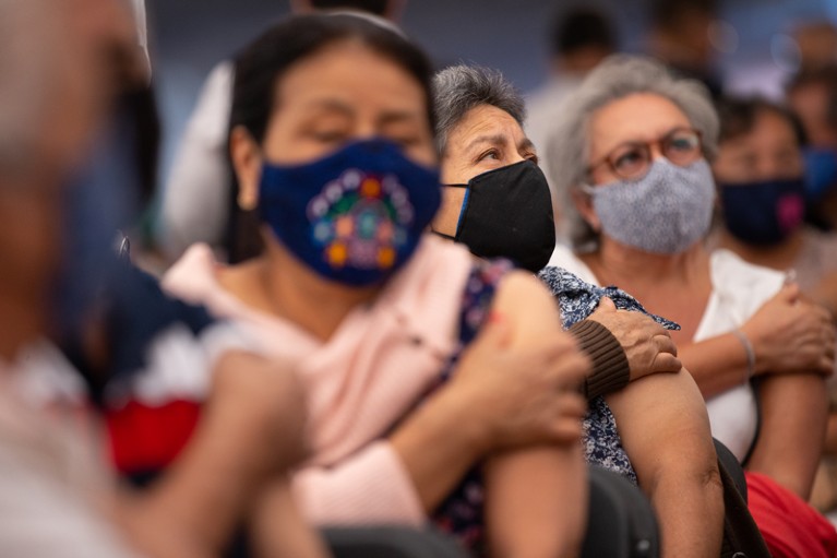 Senior citizens wearing facemasks hold their upper arms after receiving a dose of a COVID-19 vaccine