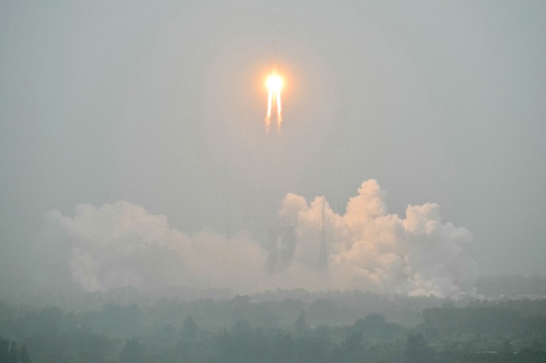 A firey orange ball hurtles over the clouds in a grey sky.