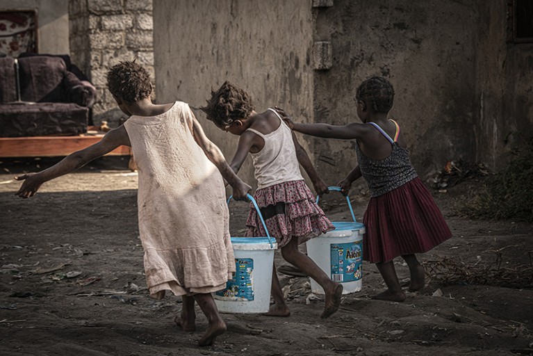 Three children carrying two large buckets of water between them
