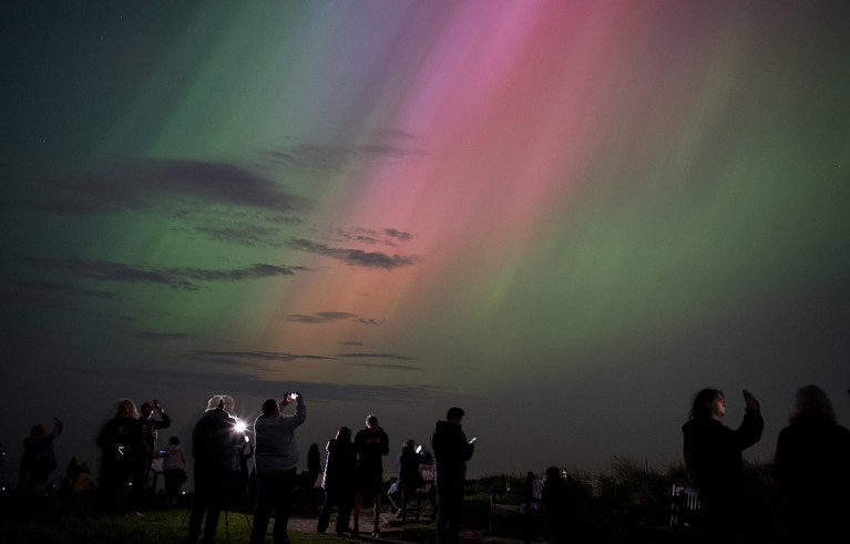 A group of people pictured beneath a sky illuminated by the aurora borealis on May 10, 2024 in Whitley Bay, England.