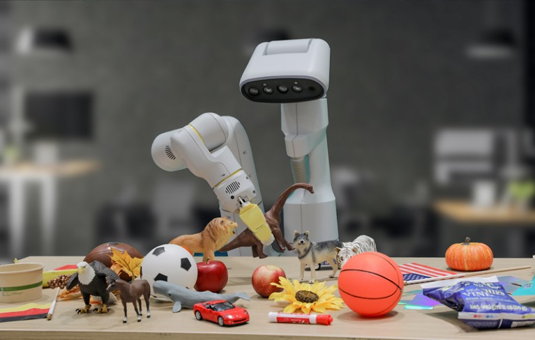 The Google DeepMind robotic arm RT-2 holding a toy dinosaur up off a table with a wide array of objects on it