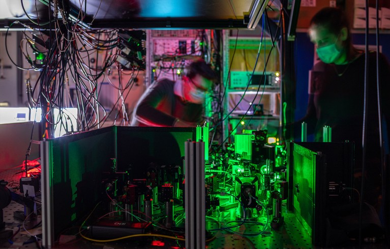 A pair of researchers work at electronic equipment lit up in green and pink.