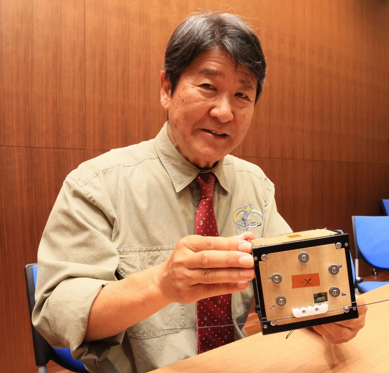 Takao Doi holds a model of the wooden artificial satellite, LignoSat.