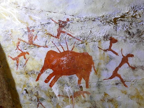 Stylized hunters gambol around an animal pierced by spears in an ancient cave painting.
