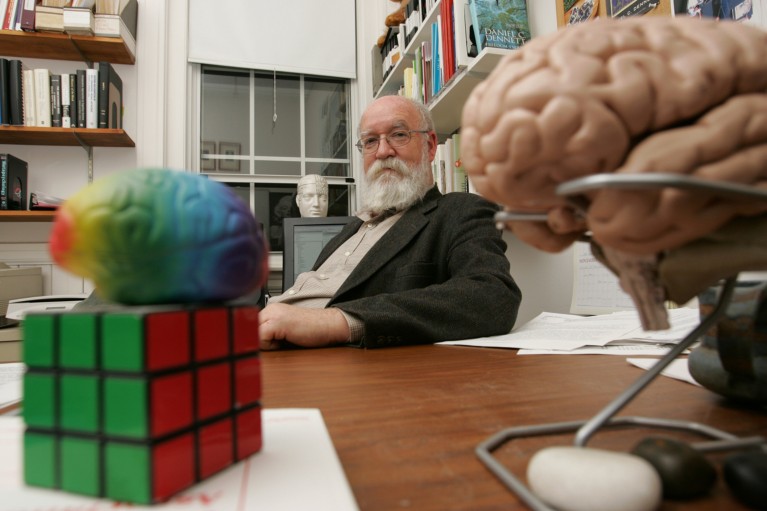 Portrait of Daniel C. Dennett in his office with models of brains in the foreground