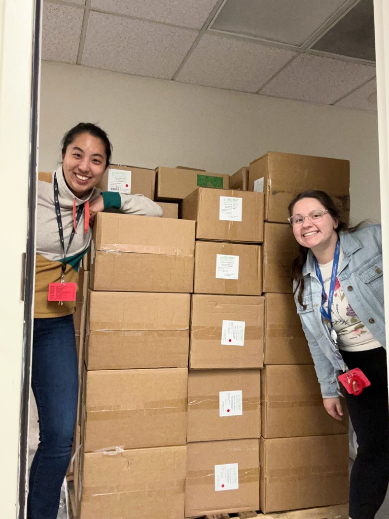 Jessica Tsai and Marissa Coppola pose for a photo next to a pallet piled high with boxes of lab supplies