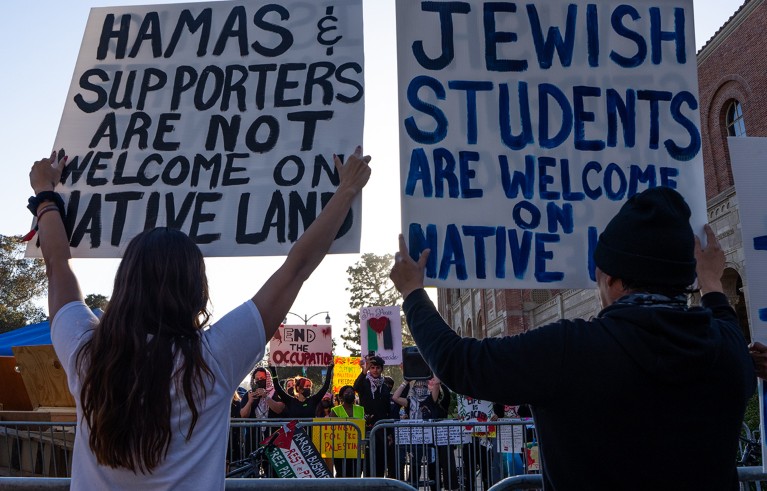 Dos estudiantes pro-israelíes y pro-palestinos sostienen carteles en un campamento en el campus de UCLA.