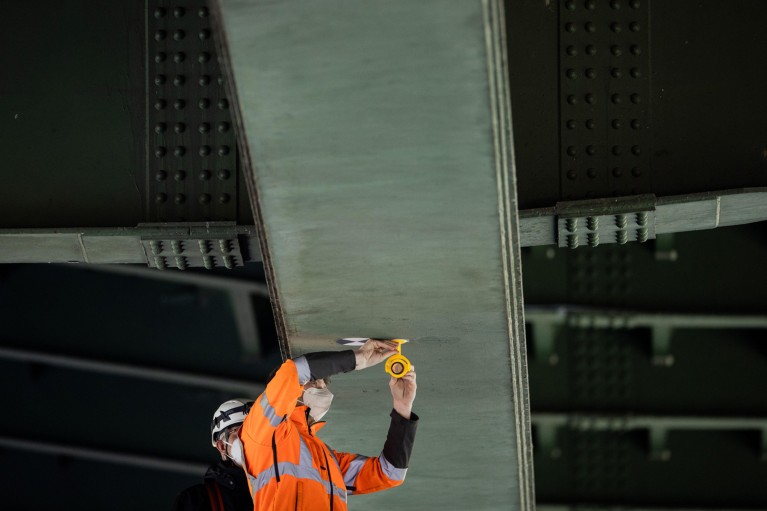 Una persona vestida con ropa naranja de alta visibilidad instala un sensor debajo del puente
