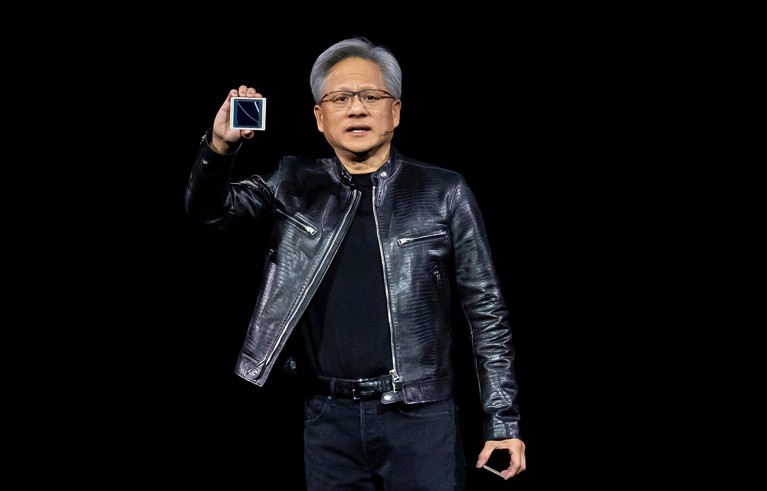 Man with a leather jacket and glasses holding a computer chip on a conference's stage.