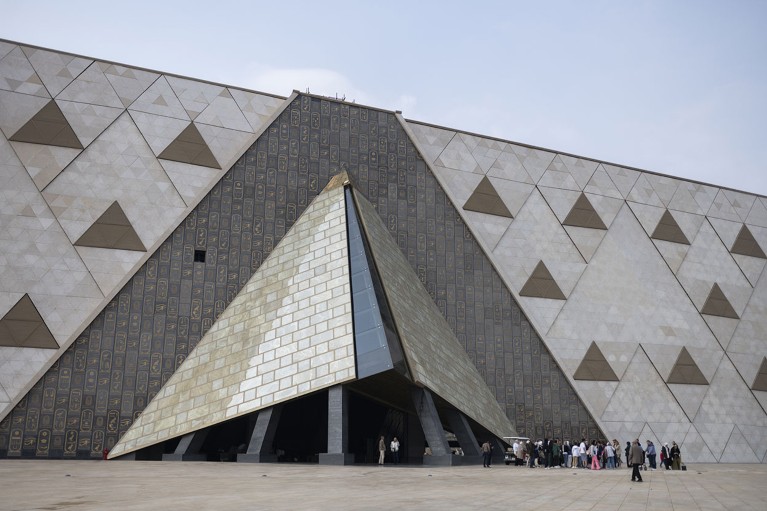 Una multitud de personas bajo la entrada del enorme museo triangular.
