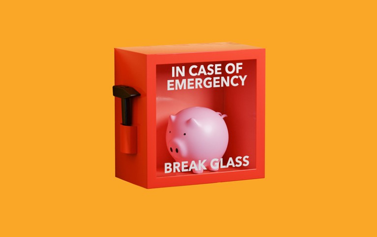 A piggy bank in a rex box with a glass window with "IN CASE OF EMERGENCY BREAK GLASS" printed on it and a hammer attached to the side