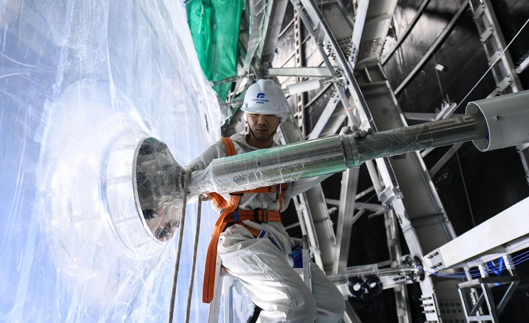 A person wearing white protective clothing and helmet, holding equipment at construction site.