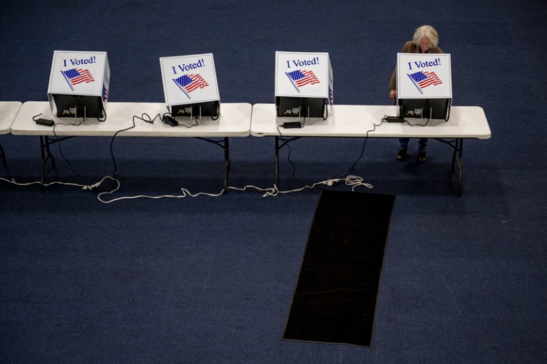 A woman registering her vote during the 2024 democratic primary at one of a bank of electronic voting machines each labeled with "I voted!" and the US flag