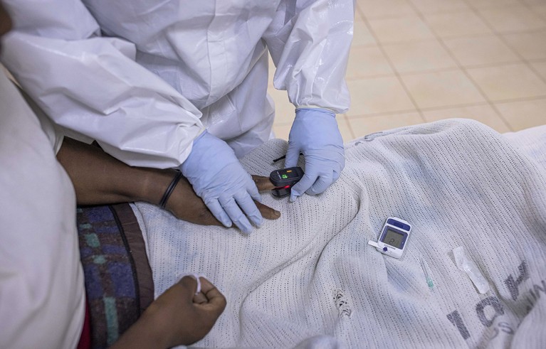 Primer plano de una enfermera ajustando el oxímetro en el dedo de un paciente negro con COVID-19 dentro de la unidad de cuidados intensivos (UCI) del Hospital Machakos Nivel 5, en Machakos, Kenia.