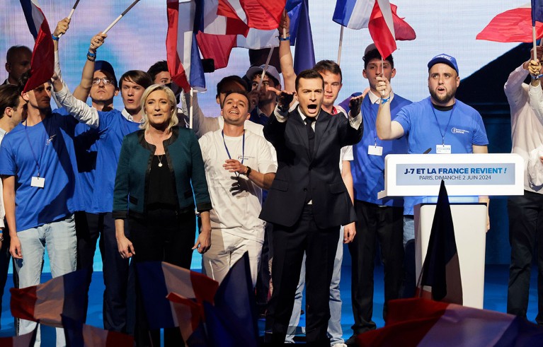 Surrounded by flag waving supporters, President of the French far-right National Rally party Jordan Bardella and the party's parliamentary leader Marine Le Pen gesture on stage during an election campaign rally.