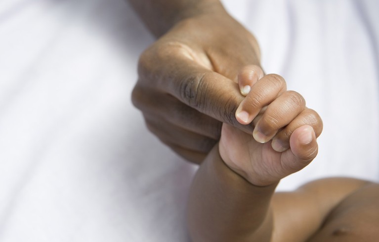 A baby's hand holding on to an adult's finger.