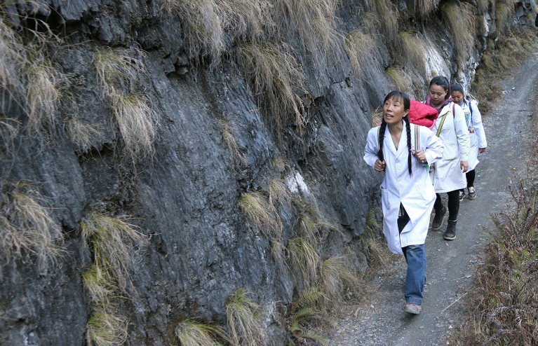 Un equipo médico camina por una carretera de montaña llevando equipo médico en la provincia de Yunnan, China.