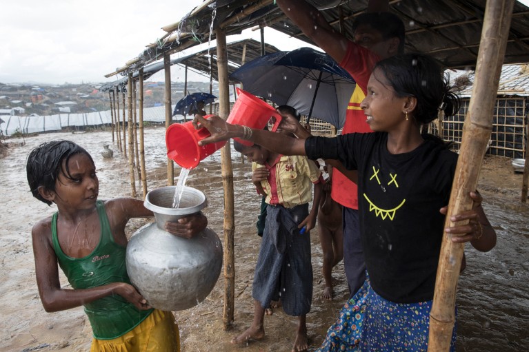 Two young girls collect rain water running off a roof and pour it into a container during monsoon rains in Bangladesh