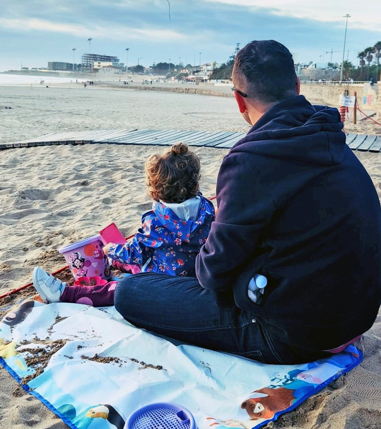 John y su hija están sentados en su lugar favorito de la playa con el resto de la familia.