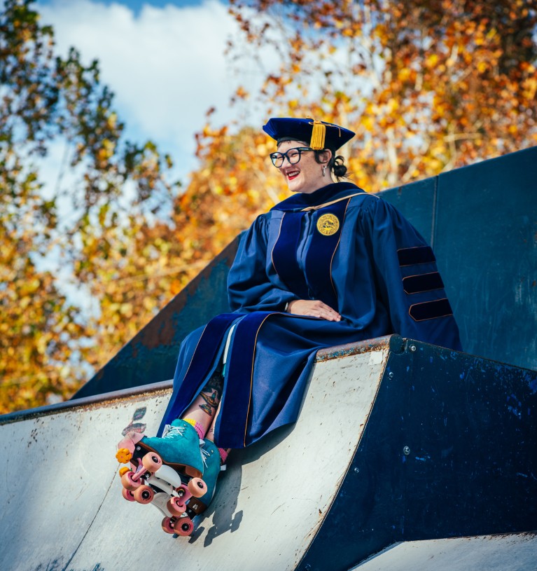 Krista Bresock sitting on top of a skate ramp wearing roller skates, graduation cap and gown