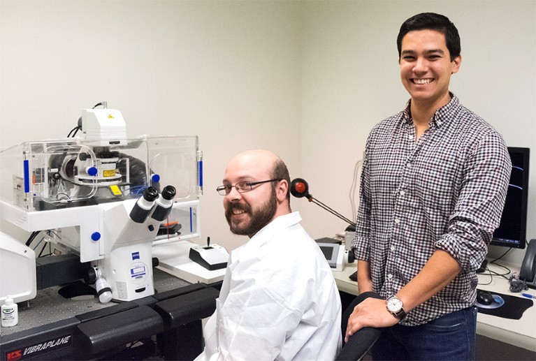 Andy Hauser (seated at microscope in a labcoat) and Craig Ramirez (standing) pictured in a laboratory