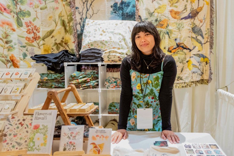 Danya Weber poses for a portrait at a market stall will cards and textiles decorated with drawings of animals and flowers