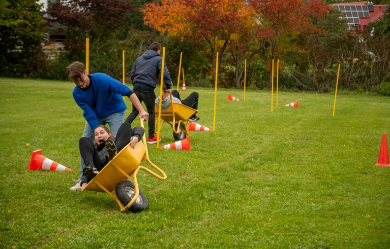 Two PhD students doing a relay race, once carrying the other in a wheel barrel on the grass.