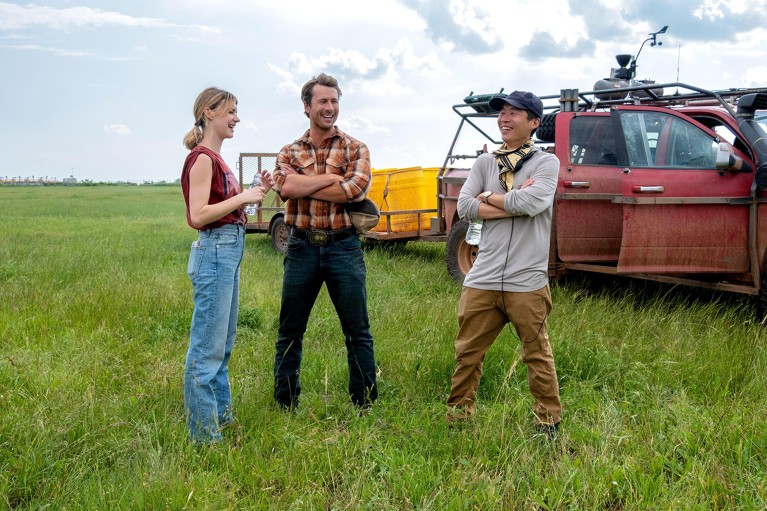 El director Lee Isaac Chung, Glen Powell y Daisy Edgar-Jones en un campo en el set de la película "tornados".