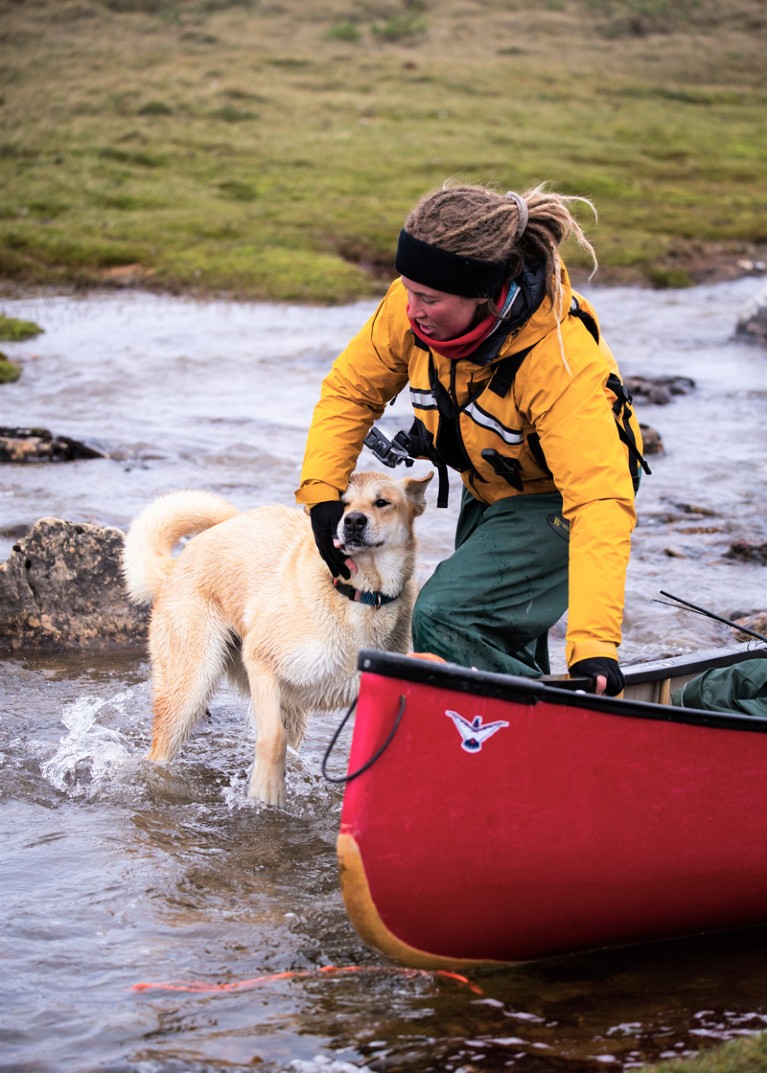 Elise Imbeau drags a canoe through a shallow waterway with one hand and holds the collar of a malamute dog with the other