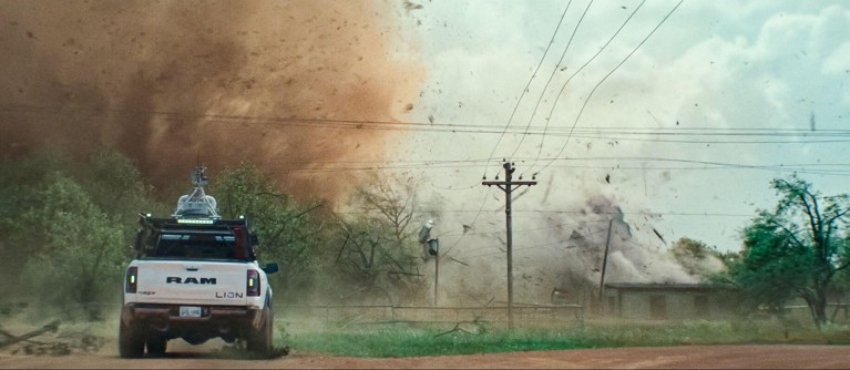 A scene from the film "Twisters" showing a truck in front of a tornado with power lines coming down nearby.