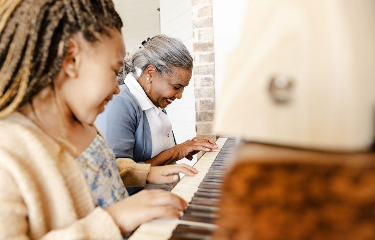 A young girl and her grandmother play a piano duet together.