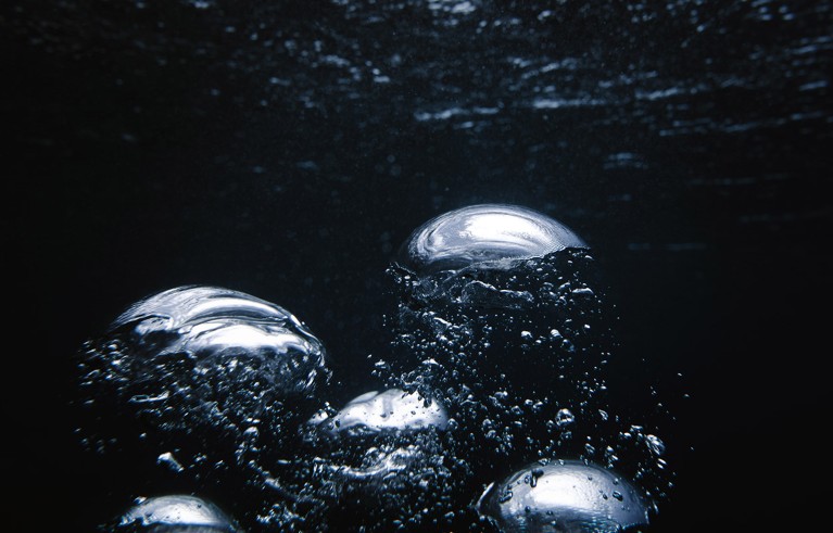 A number of large bubbles rise through dark water.