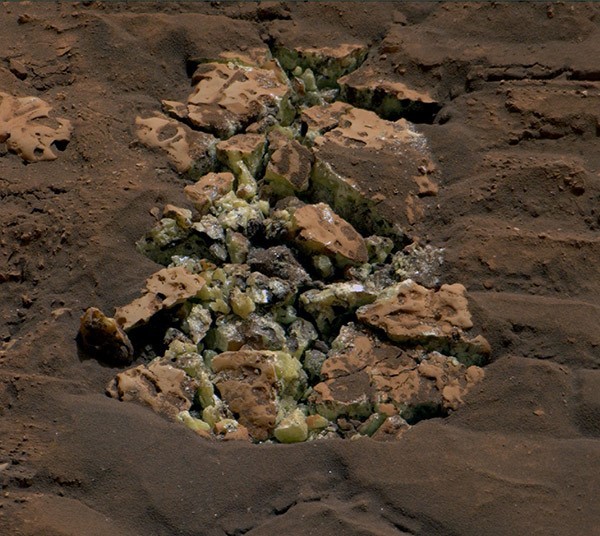 A close up view of yellow crystals of elemental sulphur spotted against the reddish brown Martian soil.