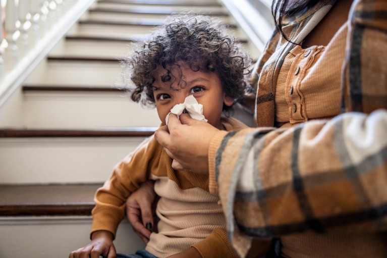 Close-up of a mother wiping a toddler's nose with tissue