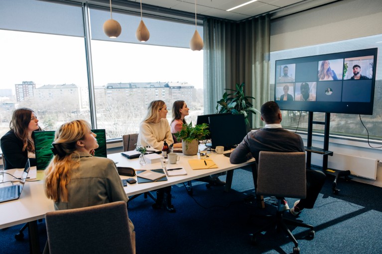 Male and female colleagues look towards a television screen during a hybrid meeting in a conference room