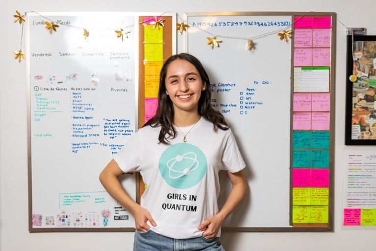 Elisa Torres Durney standing next to a white board wearing a t-shirt with "Girls in Quantum" written on it