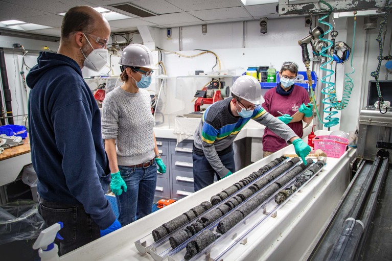 Scientists in hard hats and face masks examine core samles in a lab on board JOIDES Resolution research vessel