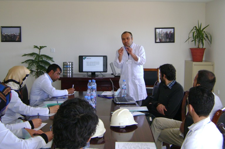 Mohammad Hadi Mohammadi stands at the head of a table teaching while people sit and listen