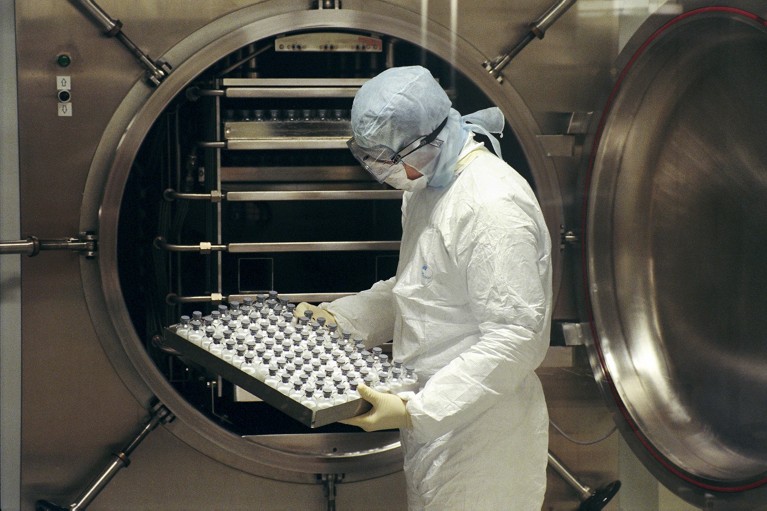 Technician placing vials of drug components in a pasteurisation machine, which separates blood plasma.